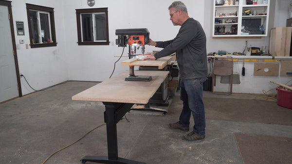 BenchBUD electric height adjustable workbench at lowest height position with drill press sitting on top. Angled side view.  