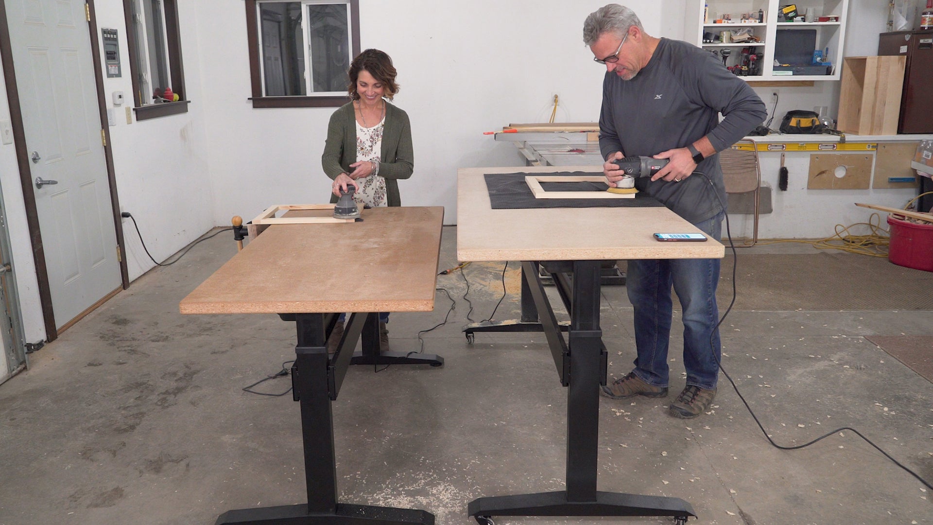 Two BenchBUD electric height adjustable workbenches side by side, each at differing heights. Showing base with top. Side view.